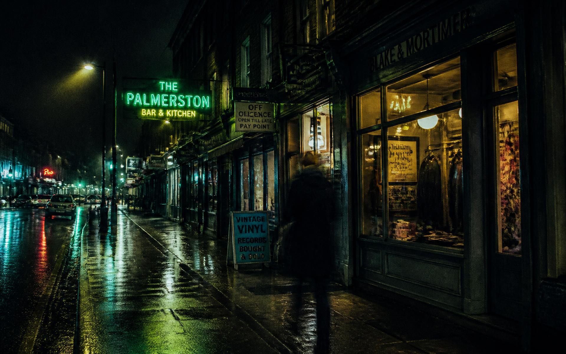 Independent shopfronts glowing along a wet British high street at dusk